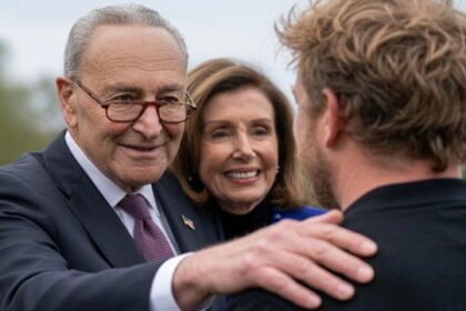 Democrats Chuck Schumer and Nancy Pelosi standing in front of Graham Platner.