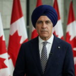Canada Prime Minister Mark carney wearing a turban in front of Canada flags.