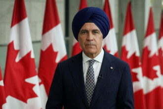 Canada Prime Minister Mark carney wearing a turban in front of Canada flags.