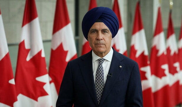 Canada Prime Minister Mark carney wearing a turban in front of Canada flags.