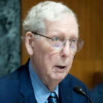 Mitch McConnell wearing a suit and tie sitting in Congress in front of a microphone.