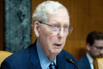 Mitch McConnell wearing a suit and tie sitting in Congress in front of a microphone.