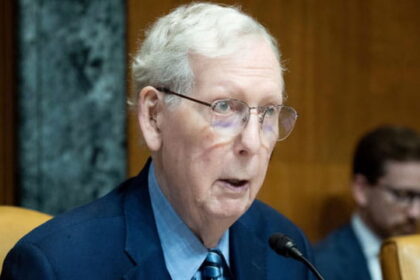 Mitch McConnell wearing a suit and tie sitting in Congress in front of a microphone.