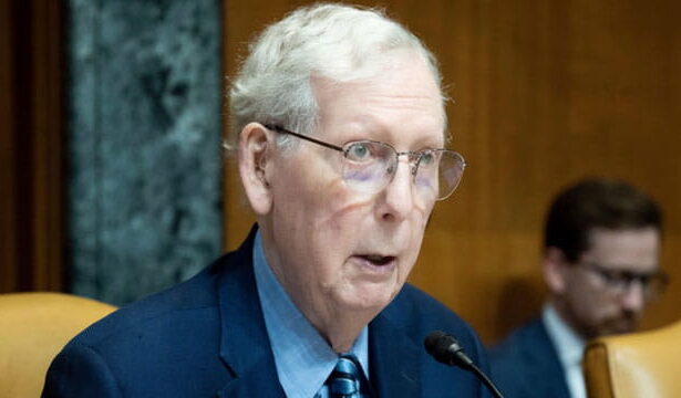 Mitch McConnell wearing a suit and tie sitting in Congress in front of a microphone.