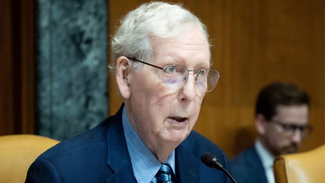 Mitch McConnell wearing a suit and tie sitting in Congress in front of a microphone.