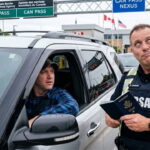 Male Canada border agent checking the passport of an American man in his car at the Canada border.