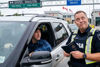 Male Canada border agent checking the passport of an American man in his car at the Canada border.