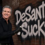 Gavin Newsom wearing all black clothes spray painting a building in Florida.