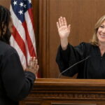White female judge wearing black robe in front of a black man inside of a courtroom.