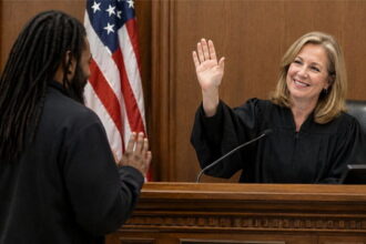 White female judge wearing black robe in front of a black man inside of a courtroom.