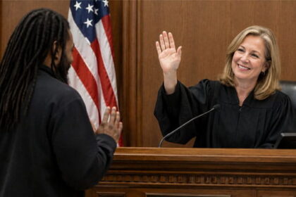 White female judge wearing black robe in front of a black man inside of a courtroom.