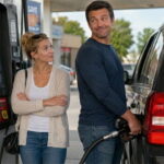 A woman watching a man fill gas in a black SUV.