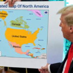 Donald Trump at his desk holding a map of North America.