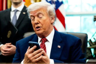 Donald Trump checking Siri on his smartphone at White House desk.