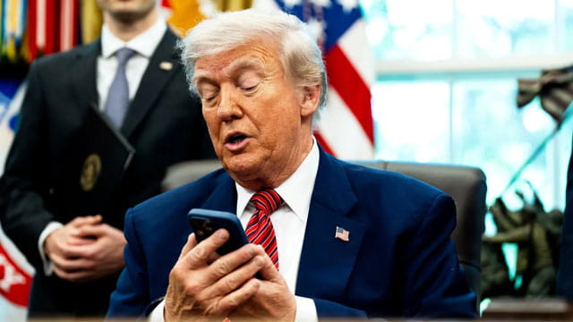 Donald Trump checking Siri on his smartphone at White House desk.
