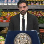 Zohran Mamdani giving a speech inside supermarket on grocery stores.