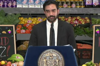 Zohran Mamdani giving a speech inside supermarket on grocery stores.