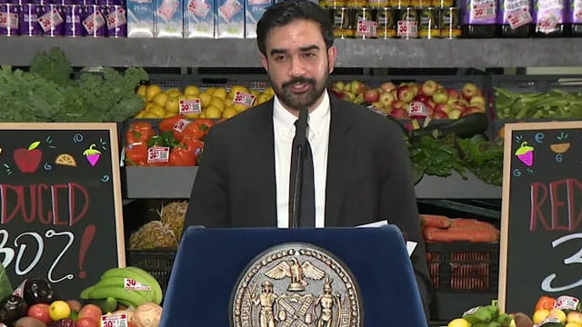 Zohran Mamdani giving a speech inside supermarket on grocery stores.