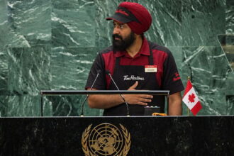 Indian Punjabi man wearing a Tim Horton's uniform giving a speech at the United Nations for Canada.