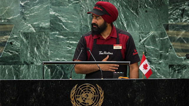 Indian Punjabi man wearing a Tim Horton's uniform giving a speech at the United Nations for Canada.