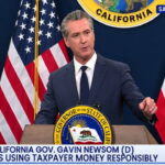 Gavin Newsom wearing a suit giving a speech on stage.