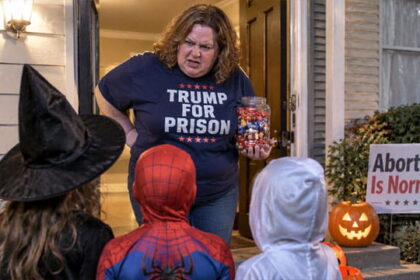 Fat liberal white woman wearing a "Trump For Prison" shirt holding a jar of candy standing in front of children wearing Halloween costumes in front of a home.