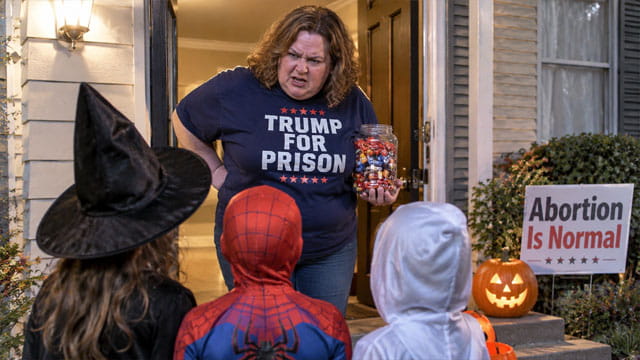 Fat liberal white woman wearing a "Trump For Prison" shirt holding a jar of candy standing in front of children wearing Halloween costumes in front of a home.