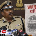 Indian male police officer wearing tan police uniform giving speech holding up a picture of a train.