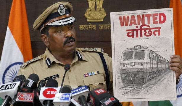 Indian male police officer wearing tan police uniform giving speech holding up a picture of a train.