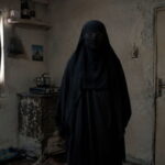 Iranian woman wearing a black burka standing in a small room.