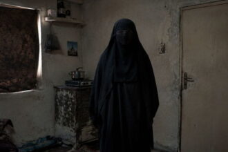 Iranian woman wearing a black burka standing in a small room.