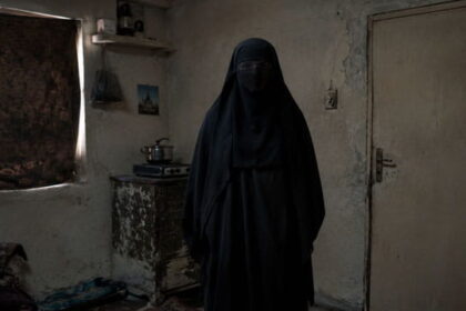 Iranian woman wearing a black burka standing in a small room.