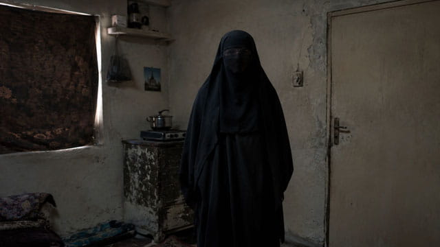Iranian woman wearing a black burka standing in a small room.
