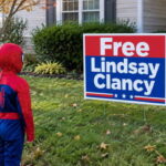 Two kids wearing Halloween costumes standing in front of a home with a "Free Lindsay Clancy" lawn sign.