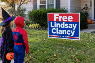 Two kids wearing Halloween costumes standing in front of a home with a "Free Lindsay Clancy" lawn sign.