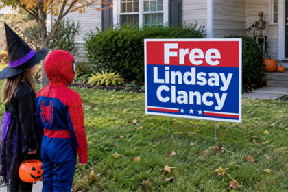 Two kids wearing Halloween costumes standing in front of a home with a "Free Lindsay Clancy" lawn sign.