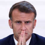 France President Emmanuel Macron wearing a suit looking pensive as he discusses French riots.