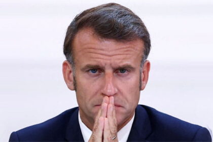 France President Emmanuel Macron wearing a suit looking pensive as he discusses French riots.