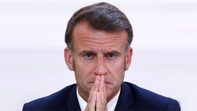 France President Emmanuel Macron wearing a suit looking pensive as he discusses French riots.