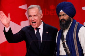 Canada Prime Minister Mark Carney standing next to an Indian Sikh man wearing a turban on stage.