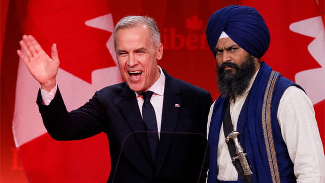 Canada Prime Minister Mark Carney standing next to an Indian Sikh man wearing a turban on stage.