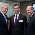 Pfizer CEO man in suit standing in the middle of two other suited executives in a boardroom.