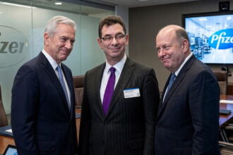 Pfizer CEO man in suit standing in the middle of two other suited executives in a boardroom.