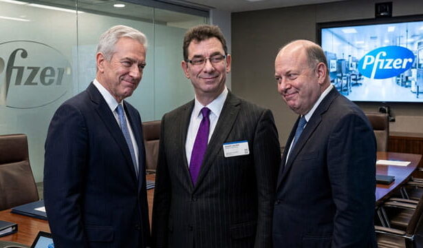 Pfizer CEO man in suit standing in the middle of two other suited executives in a boardroom.