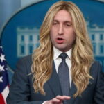 Trump Chief of Staff Stephen Miller wearing a long blonde wig speaking behind a White House Press Secretary podium.