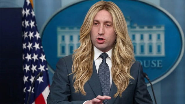 Trump Chief of Staff Stephen Miller wearing a long blonde wig speaking behind a White House Press Secretary podium.