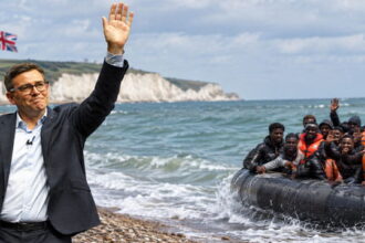 UK Prime Minister Andy Burnham waving to a group of African migrants on a boat.