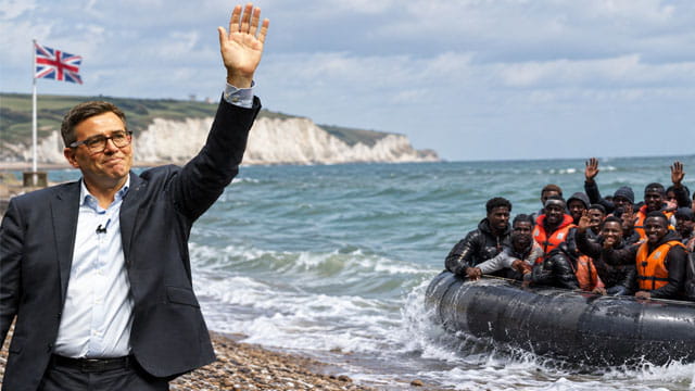 UK Prime Minister Andy Burnham waving to a group of African migrants on a boat.