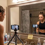 Female fitness influencer wearing gym clothes staring into a mirror for a TikTok video.